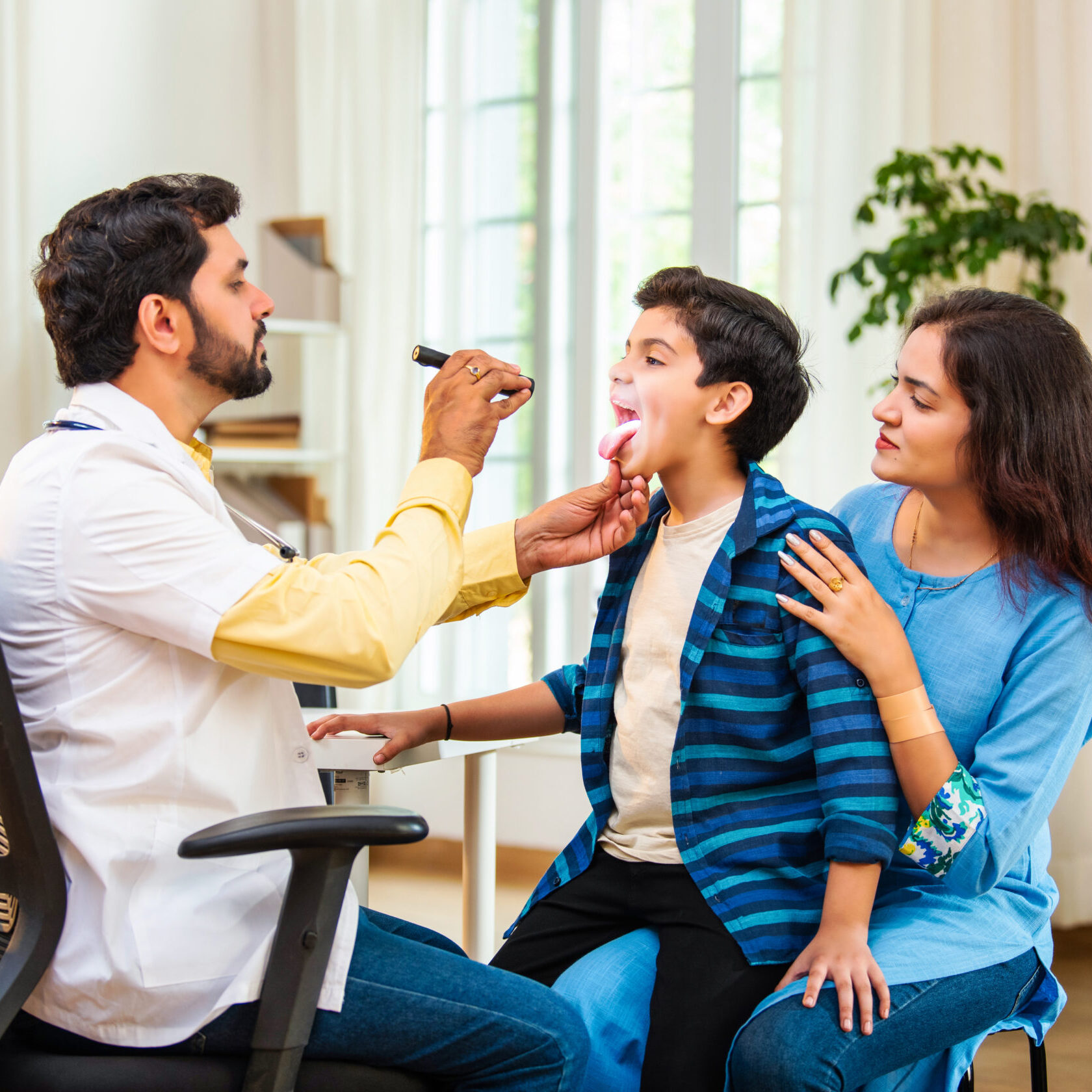 indian doctor examining young boy with stethoscope as mother observes in a modern clinic